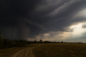 Dramatic storm and microburst cloud with rain over country road in rural area