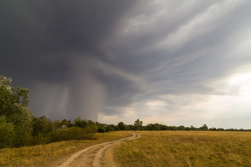 Dramatic storm and microburst cloud with rain over country road in rural area