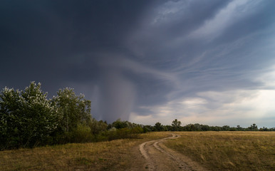Dramatic storm and microburst cloud with rain over country road in rural area