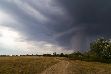 Dramatic storm and microburst cloud with rain over country road in rural area