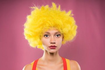 Sad girl clown in yellow wig on pink background