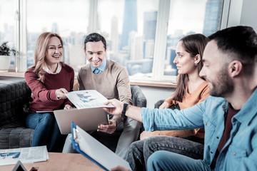 Fototapeta premium Important document. Friendly responsible pleasant office workers sitting on the sofa observing the document and using the laptop.