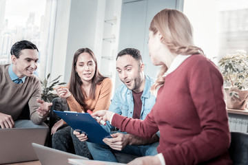 Interesting detail. Four young interested clever people working in the office sitting near the window and focusing on the document.