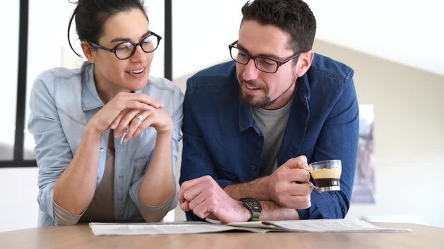 Couple with eyeglasses reading newspaper at home