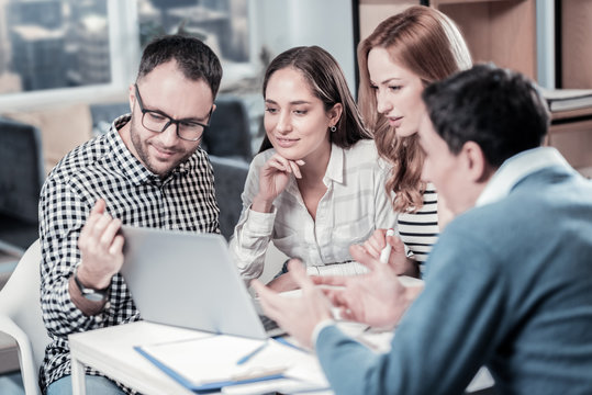 Collective creativity. Four smart occupied concentrated workers sitting together in the room using the laptop and looking at the screen.