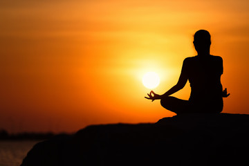 Silhouette of young asian woman practicing yoga on the beach at sunset.relaxing concept.