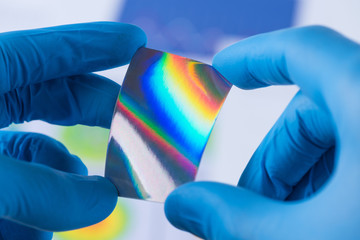 Piece of new type of material or thin coating on plastic with improved properties in laboratory in scientist hands, iridescent and pressure sensitive