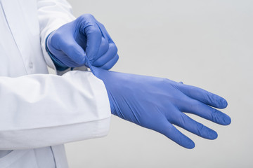 Doctors hands. Close up of handsome male arms trying to fit in one time gloves while standing on the isolated background