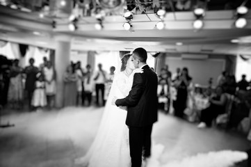 Beautiful wedding couple kissing and danicng in the restaurant during their wedding party. Black and white photo.