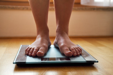 Female bare feet with weight scale on wooden floor