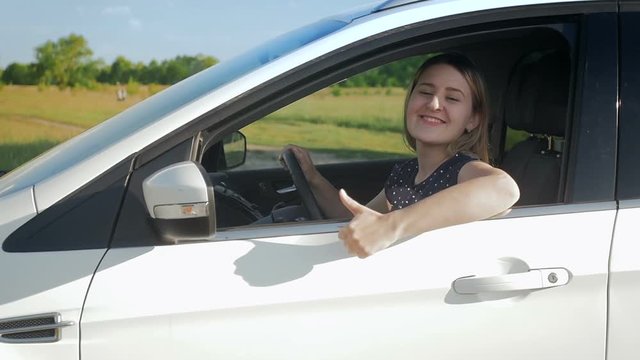 Slow motion footage of happy smiling woman driving car at sunny day and showing thumbs up