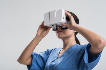 Sensitive world. Good looking energetic female doctor  holding VR glasses and putting it on head  while preparing to perform  virtual surgery
