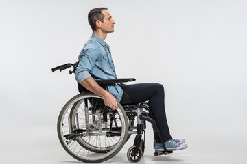 New start. Thoughtful concentrated handicapped man touching wheels and sitting in profile while...
