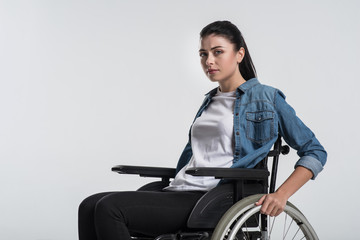 Future ahead. Young budding crippled woman looking at the camera while using wheelchair and waiting