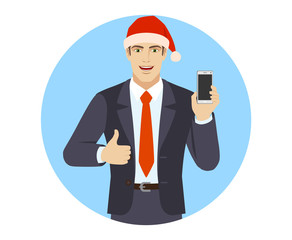 Businessman in Santa hat with mobile phone showing thumb up