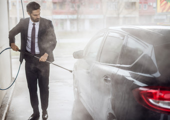 Portrait view of stylish focused serious bearded young hardworking confident man in suit washing...
