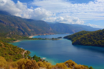 Fototapeta premium Amazing aerial view of Blue Lagoon in Oludeniz, Turkey. Summer landscape with mountains, green forest, azure water, sandy beach and blue sky in bright sunny day. Travel background. Top view. Nature