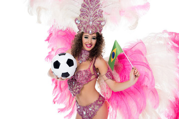 smiling woman in carnival costume holding football ball and brazilian flag while looking at camera, isolated on white