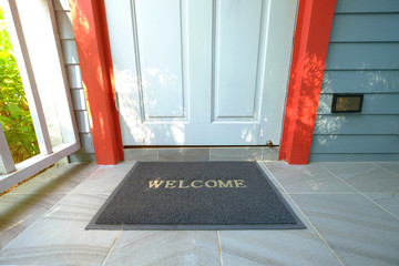 Welcome doormat in front of the wooden door nearby a green garden