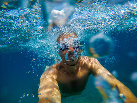 Underwater view of a young playful man relaxing and snorkelling at the sea for summer holidays while taking a selfie.