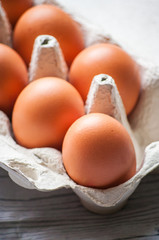 Close-up view of raw chicken eggs in egg box on white wooden background