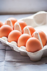 Close-up view of raw chicken eggs in egg box on white wooden background