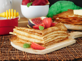 A pile of crepes decorated with a strawberry and a fig. Breakfast on a wooden background