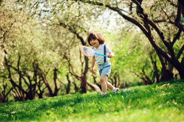 happy 3 years old child boy catching butterflies with net on the walk in sunny garden or park. Spring and summer outdoor activities, happy childhood concept.