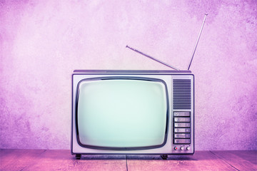 Retro old TV set receiver on table front textured concrete wall background. Vintage style filtered photo