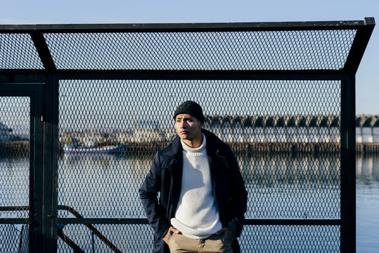 Stylish man leaning on fence at water