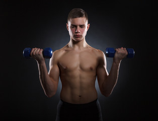 Fototapeta na wymiar Muscular young man with dumbbells on a dark background.