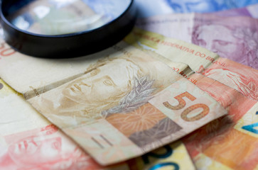 Notas de dinheiro acompanhado de moedas, carteira de trabalho, lupa, calculadora encima da mesa