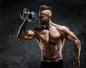 Athletic man doing exercises with dumbbells at biceps. Photo of strong male with naked torso on...