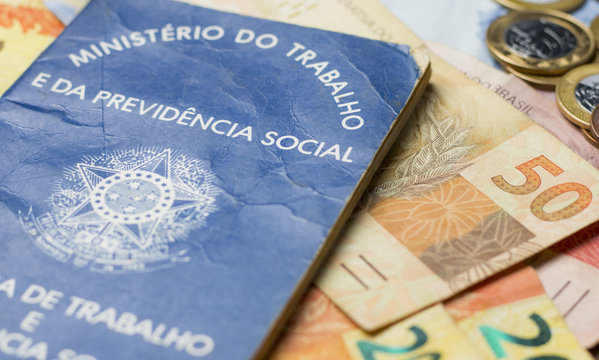 Notas de dinheiro acompanhado de moedas, carteira de trabalho, lupa, calculadora encima da mesa