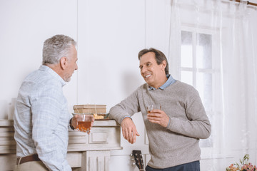 Two men with glasses in hands speaking near wall in room