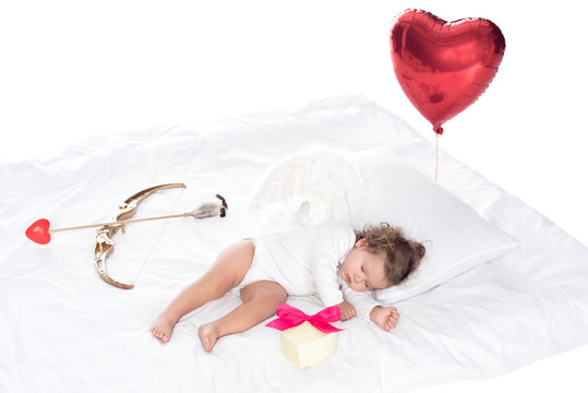 little cherub with wings lying on bed with heart balloon, present, bow and arrow, isolated on white