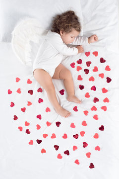 cupid with wings sleeping on bed with red hearts