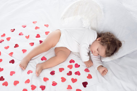 little cupid with wings sleeping on bed with red hearts