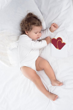 little cherub with wings lying on bed with hearts