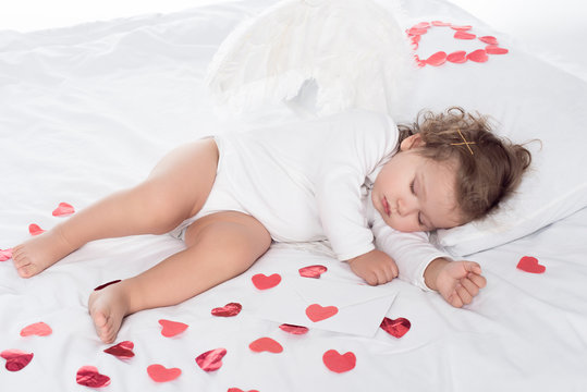 little sleepy cherub with wings lying on bed with hearts
