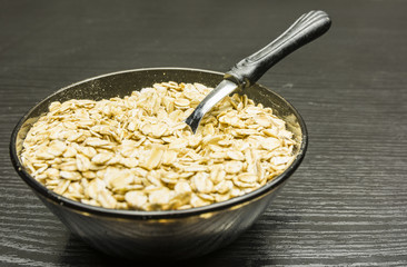 Bowl of dry rolled oat flakes oatmeal on old wooden table