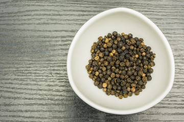 Whole peppercorns in a white bowl.