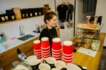 Portrait of hipster friendly female barista with many disposable red cups on coffee machine. Top view. Coffee business owner concept.