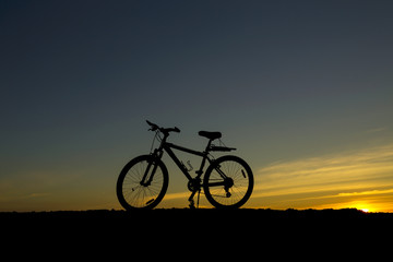 Silhouette bicycle on the hill at sunset.