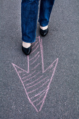 Woman in shoes standing on the asphalt road. On the road with chalk drawn signs arrows.

