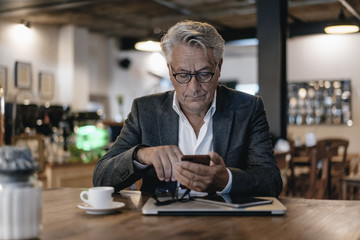 Senior businessman sitting in cafe, checking messages on smartphone