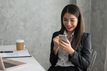 Fototapeta premium Excited asian business girl while reading a smart phone sitting in her workstation. Business Success Concept