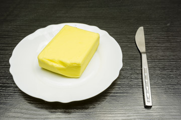 Butter on a white plate and a knife on the table.