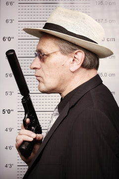 Dangerous criminal man portraited with silenced pistol in front of mug board