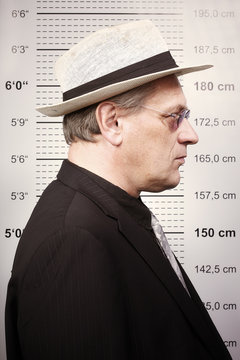 Criminal man in sunglasses and hat in front of mug board